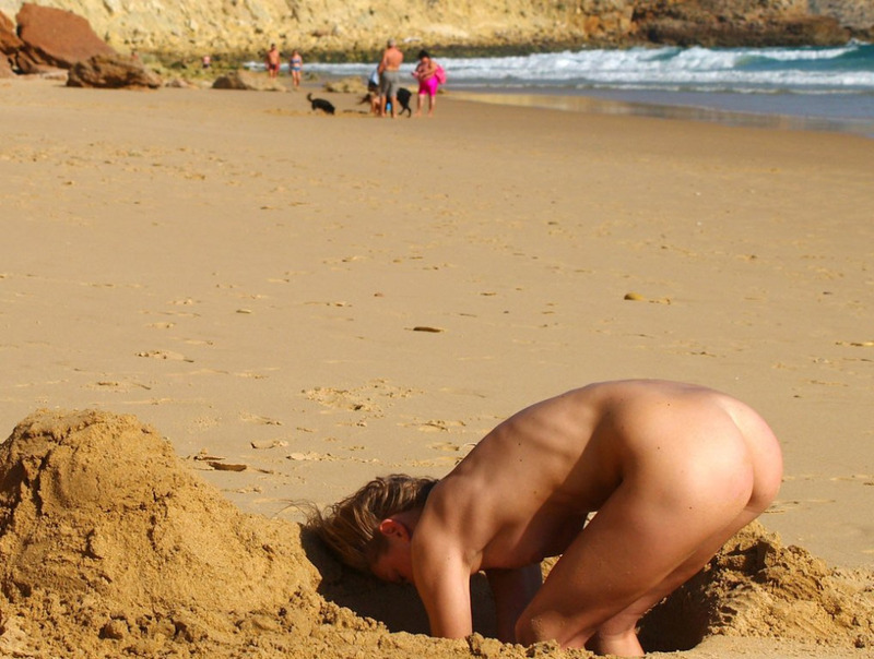 Голая блондинка играется на пляже в песке